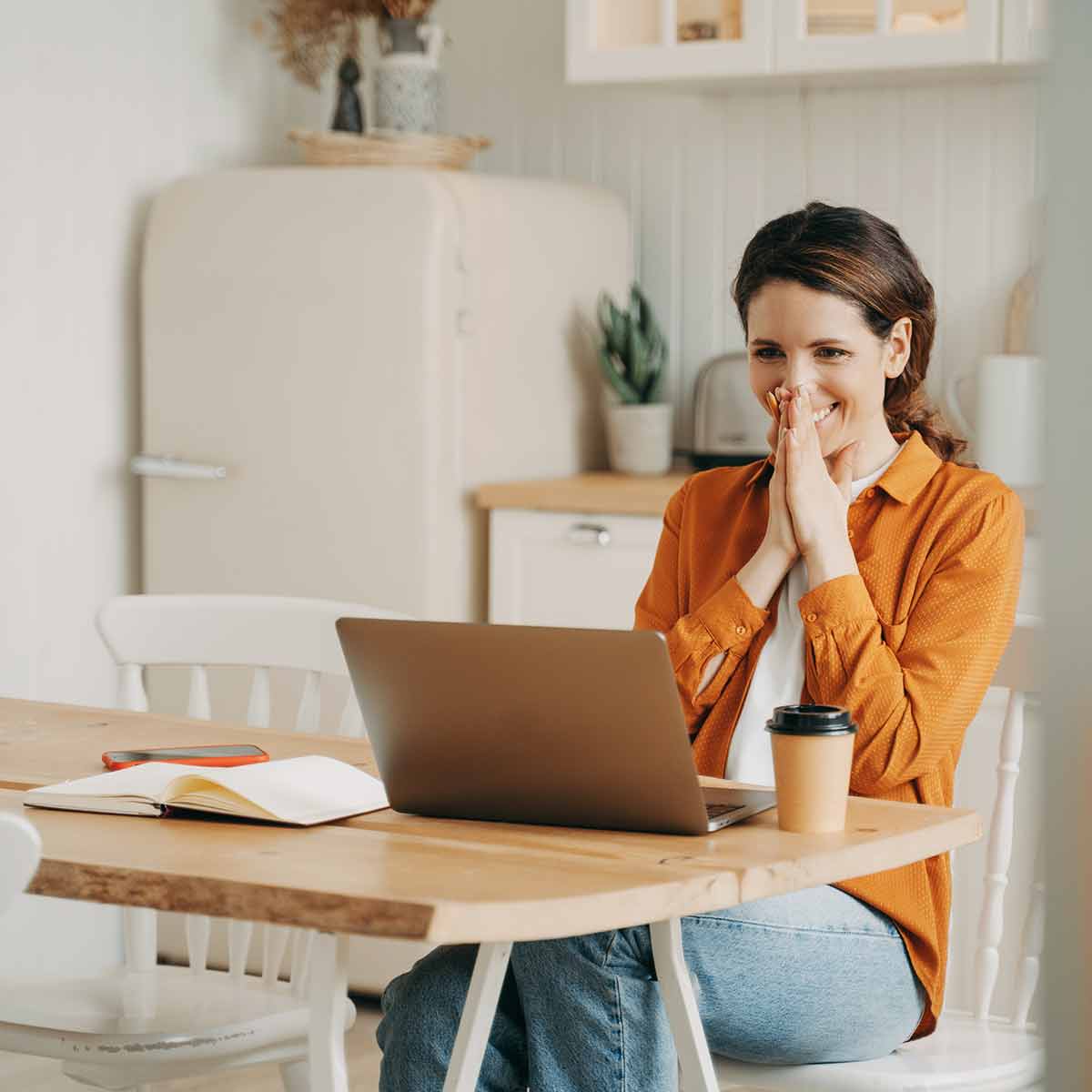 Woman seated in her kitchen looking at her computer - happy about the product she’s found on the Built for Home Product Guide website.
