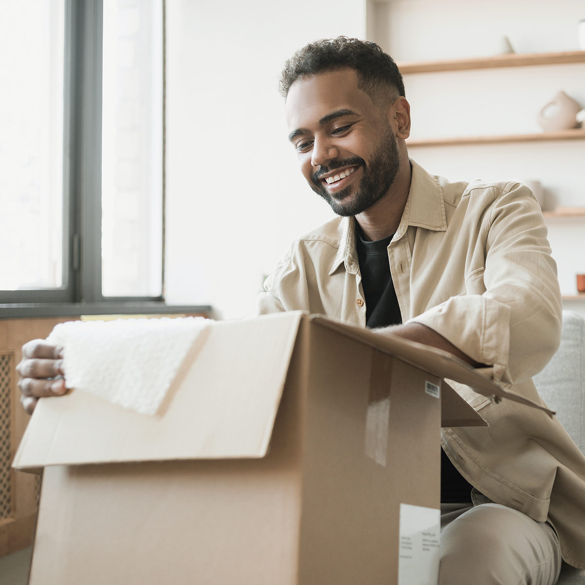 Man sitting on a sofa is happy to open an affiliate gift from a home product manufacturer.