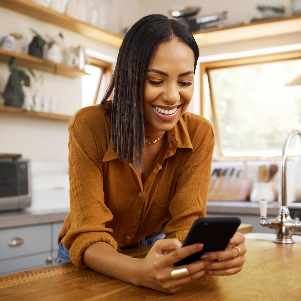 Happy woman leans on counter in kitchen reading a text message on her phone.