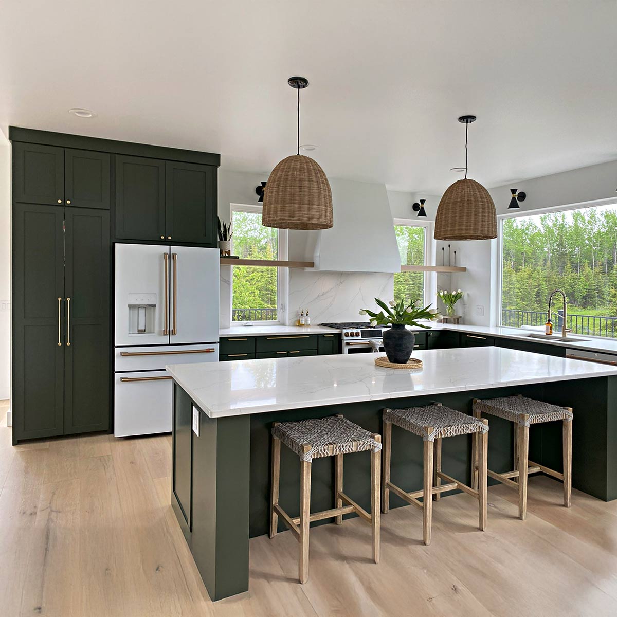 Dark green shaker kitchen cabinet doors with gold hardware set against a white and bright kitchen.