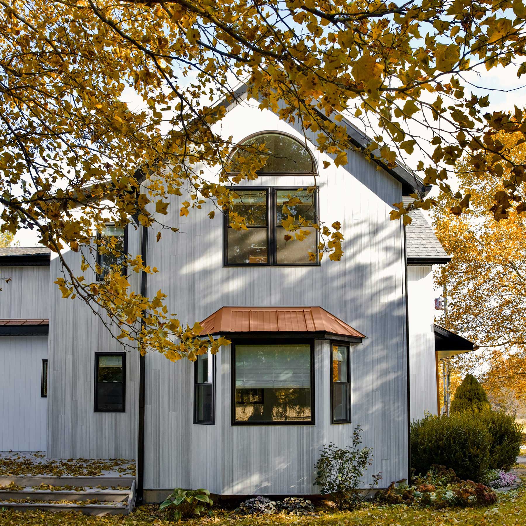Modern house with light colored exterior cladding and autumn foliage.